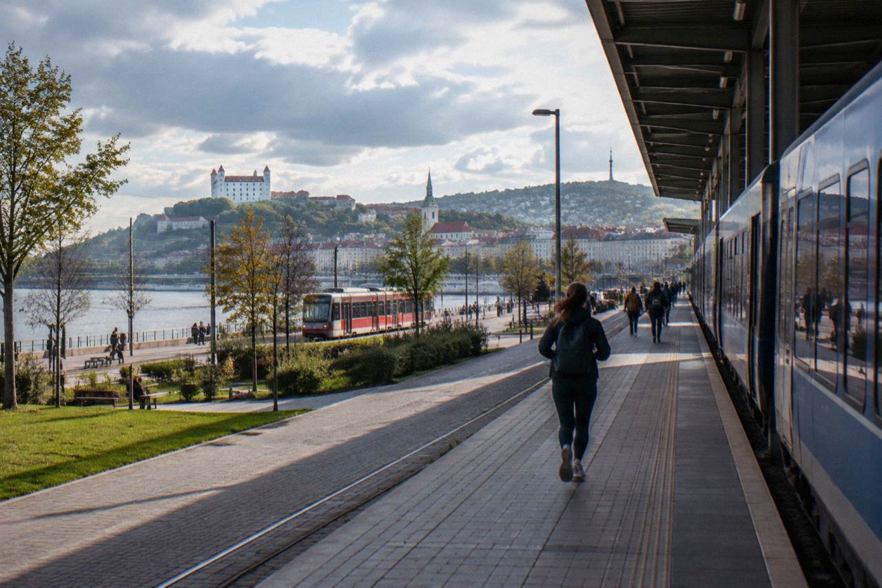 A regional train standing at a platform beside a river city skyline