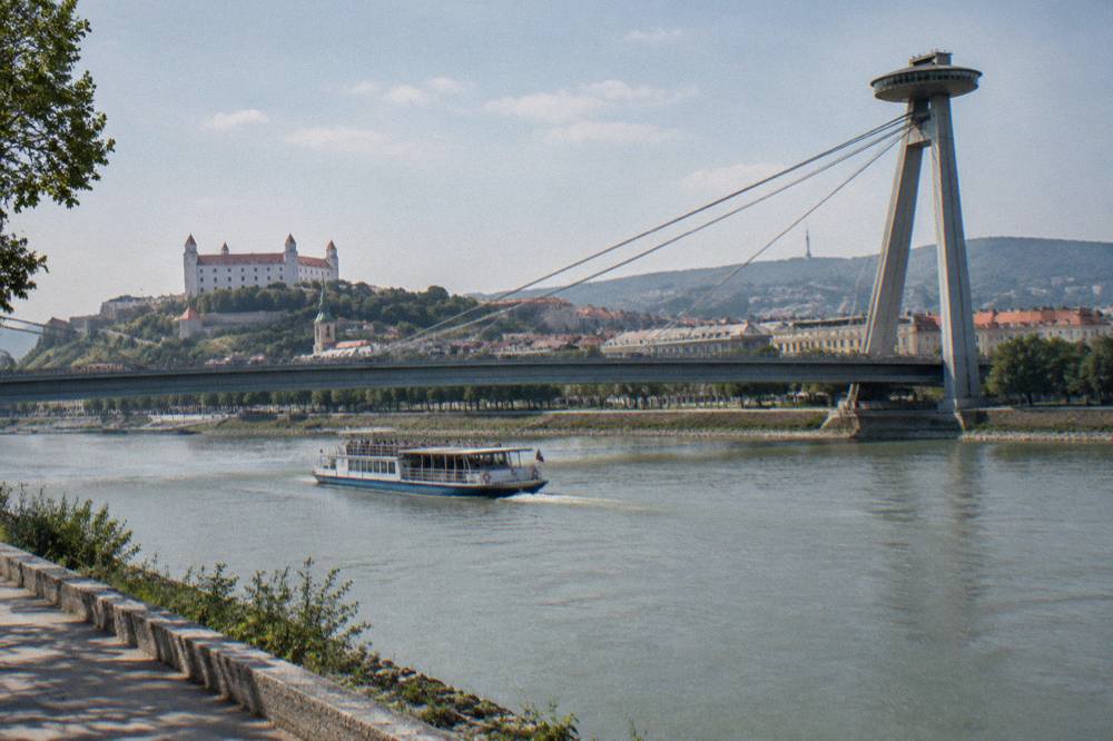 Open-deck boat cruising on the Danube past Bratislava's riverfront and UFO bridge