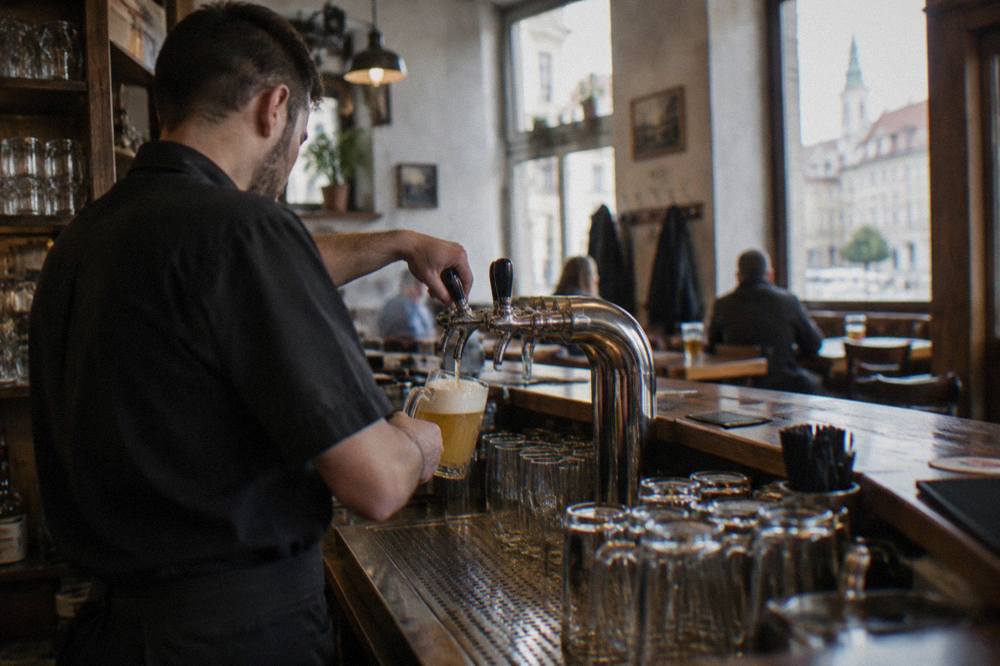 A bartender pouring draft beer behind the counter of a small Bratislava pub