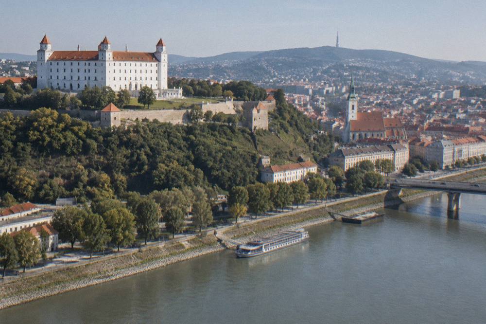 Bratislava Castle standing above the riverfront, white walls and tiled roofs under a clear sky
