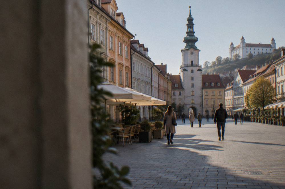 People walking across the main square of Bratislava Old Town past coloured townhouses