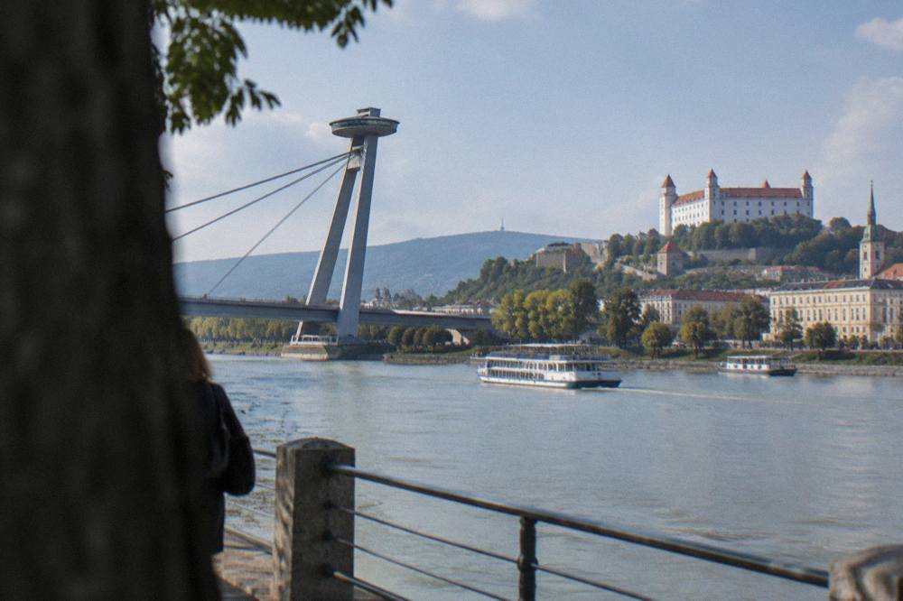 View from a riverbank walkway towards the Most SNP bridge with its UFO deck, with boats on the Danube below