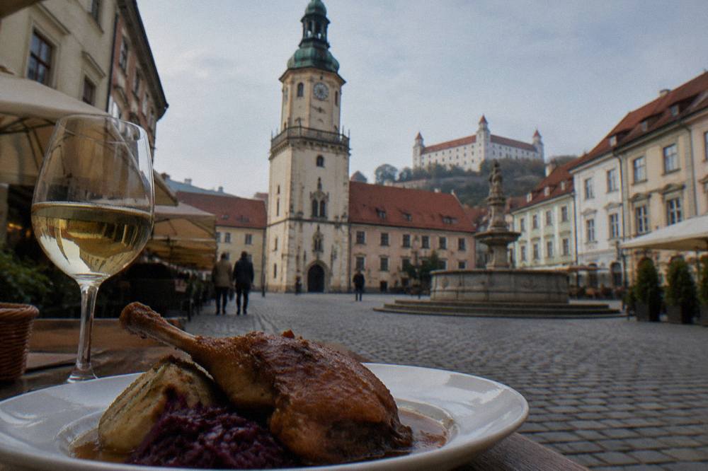 A glass of white wine and a plate of roast goose with cabbage on a table in a Small Carpathian wine cellar