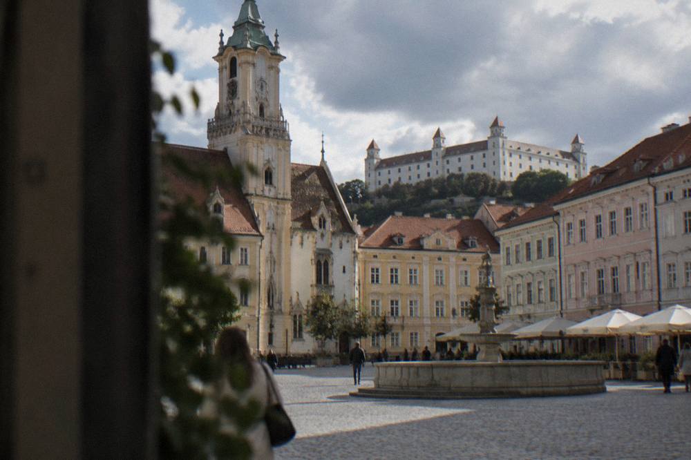 A hilltop castle seen from a town square with coloured facades below