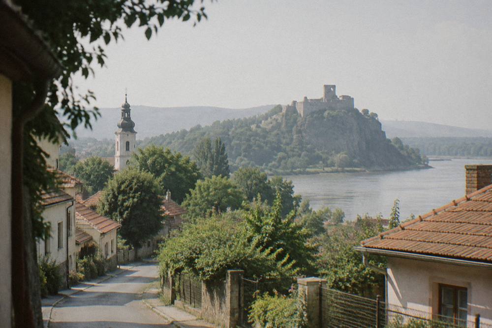 A village street with low houses and a church tower among green trees