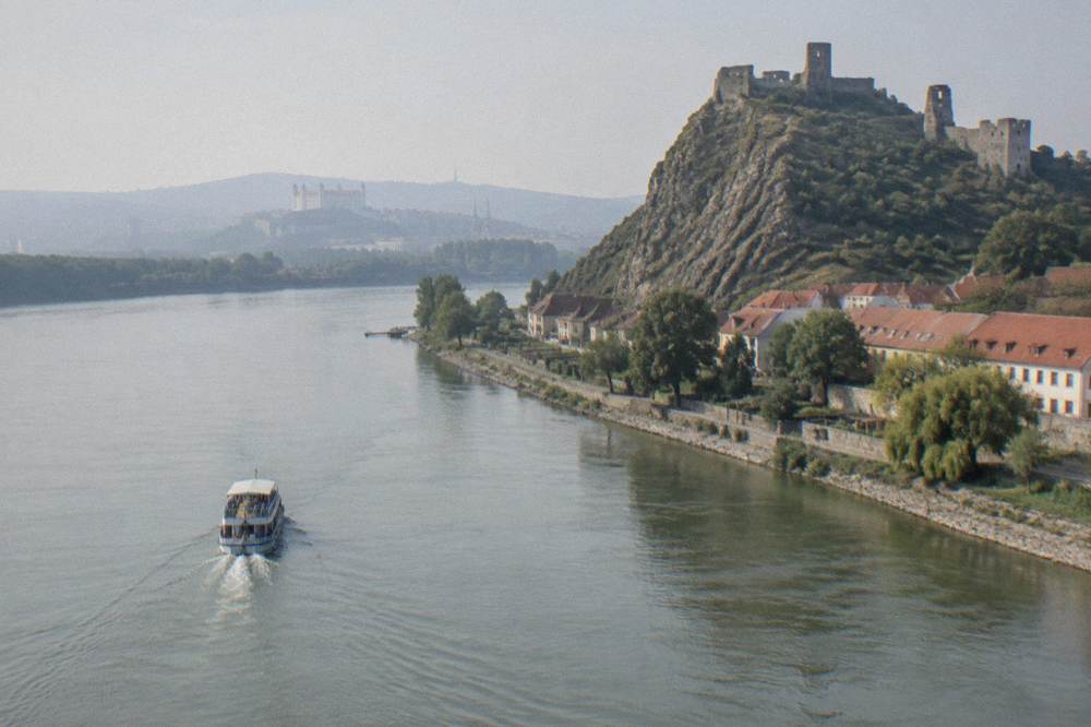 A boat on a wide river with a castle hill coming into view ahead