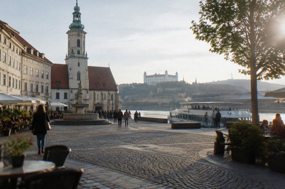 A river boat moored at a city pier with passengers boarding on a bright morning