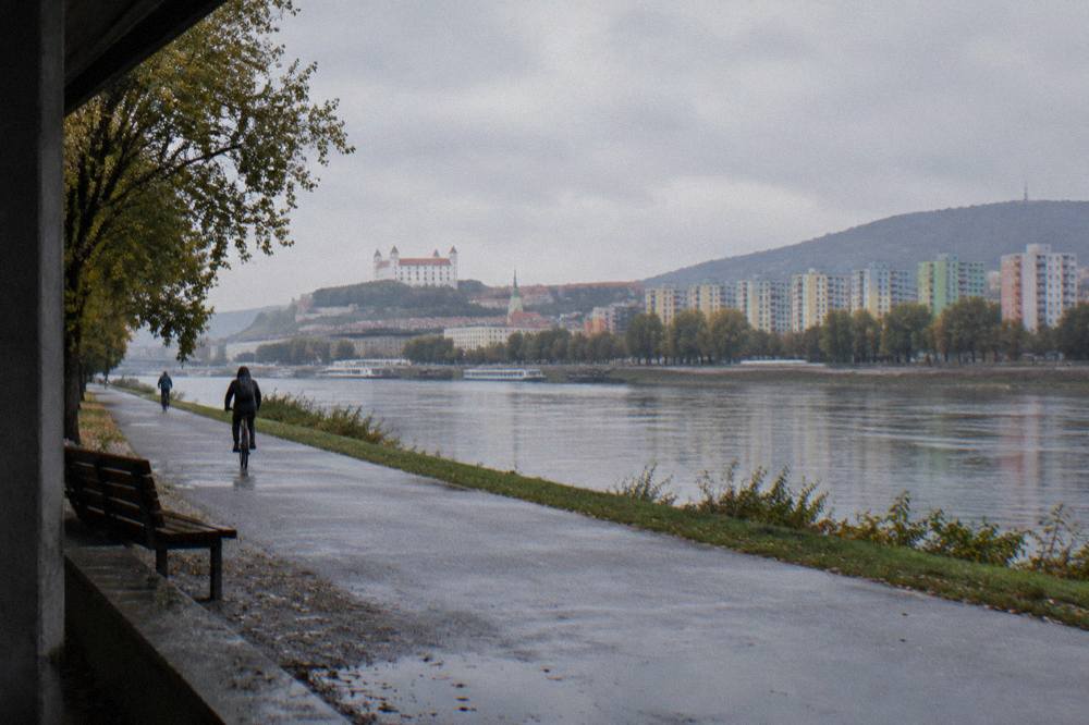 A pedestrian path along the Danube with apartment towers and trees on the far bank