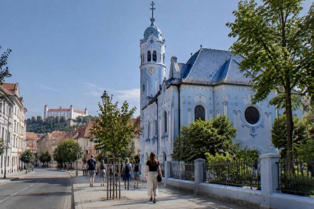 Tourists walking on the pavement outside the blue facade of the Church of St Elizabeth