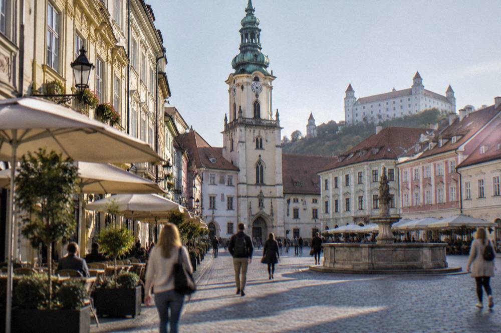 Tourists walking through a narrow street in Bratislava past cafes and old facades