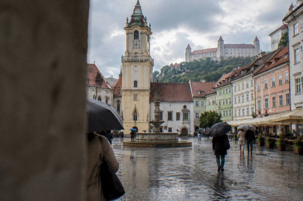 A rainy cobblestone street in Bratislava with umbrellas and reflections