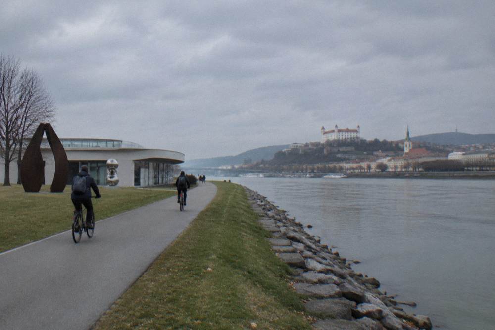 Cyclists on a riverside path with the wide Danube in view