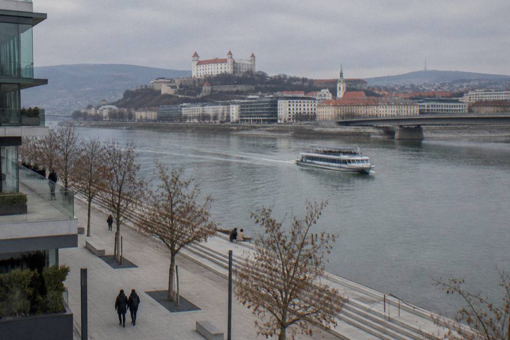 A passenger boat cruising on the Danube with a bridge and riverside buildings behind it in Bratislava