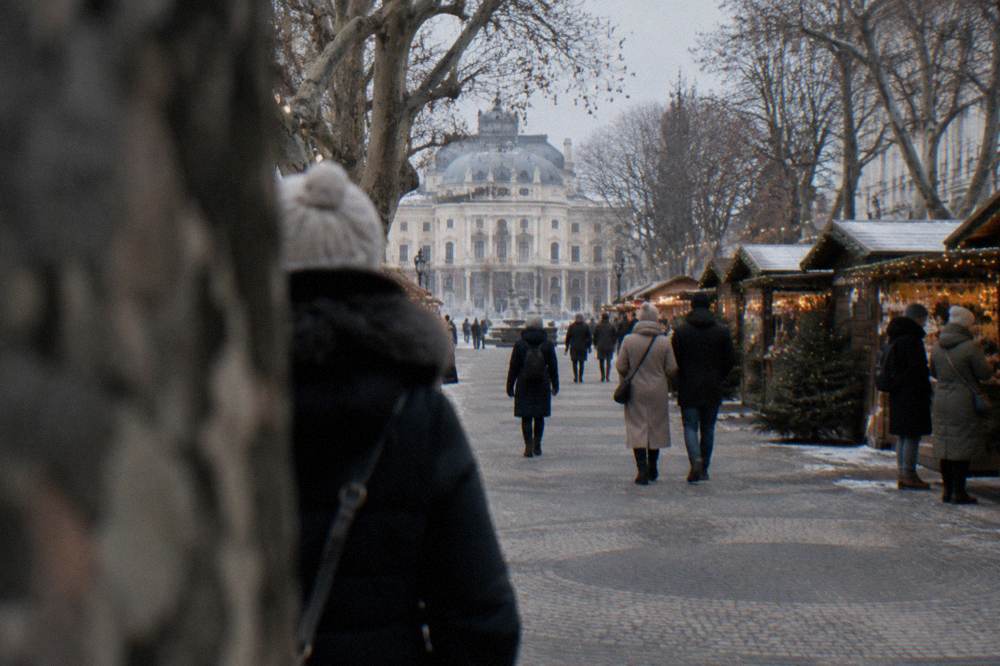 A Christmas market with wooden stalls and lights under trees on a city square