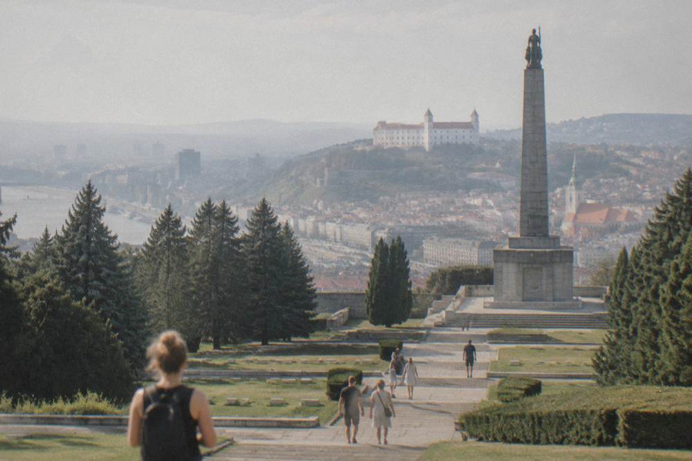 Visitors walking up stone steps between terraced lawns toward a tall memorial column