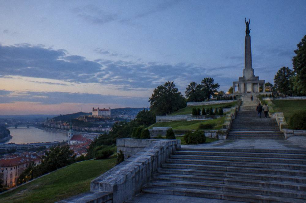 A wide stone staircase and formal terrace leading up a green hillside toward a monumental column