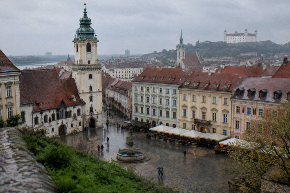 A panoramic view over rooftops and church towers of a city centre from a green hillside