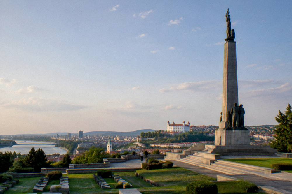 A monumental stone column and sculpture seen from below against an evening sky