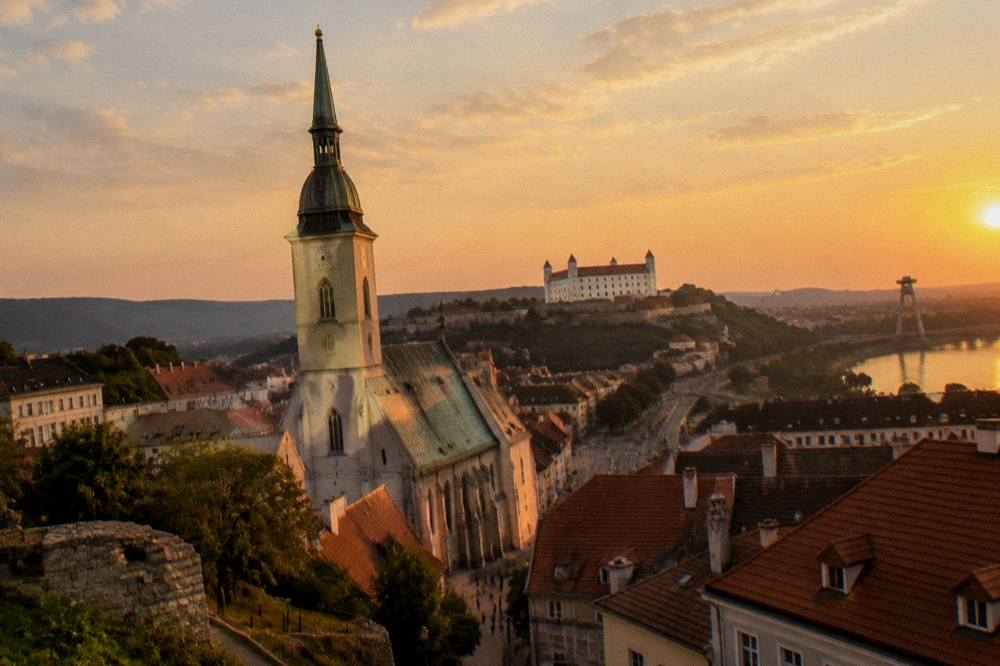 Evening view of an illuminated Gothic church tower above city rooftops