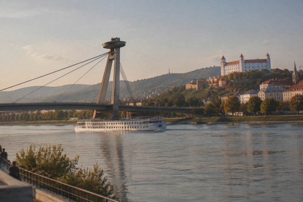 A river cruise boat passing under the SNP bridge near the UFO tower in Bratislava