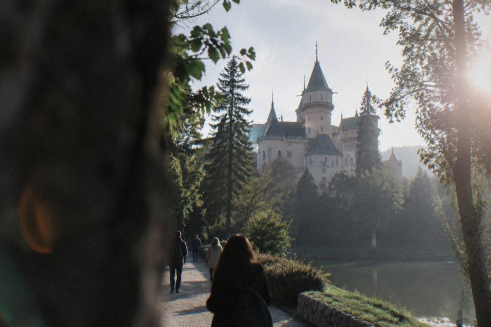 Tourists walking on a path through parkland toward a castle with pointed towers