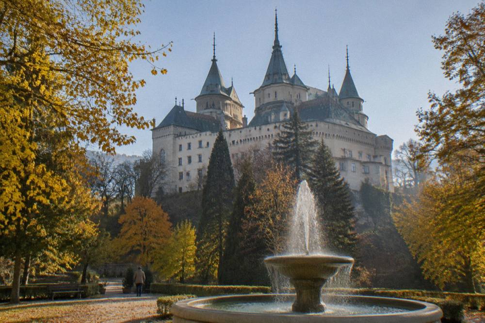 A castle garden in autumn with orange and yellow trees around a fountain