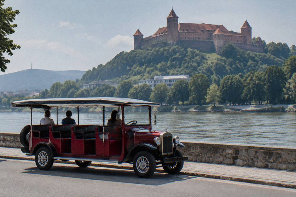 A vintage open-sided sightseeing vehicle parked on a Bratislava street near the Danube