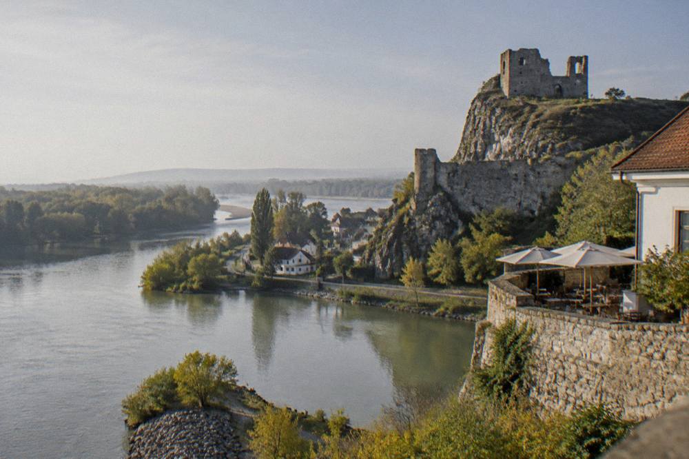 Stone castle walls above the water with a small cafe terrace nearby
