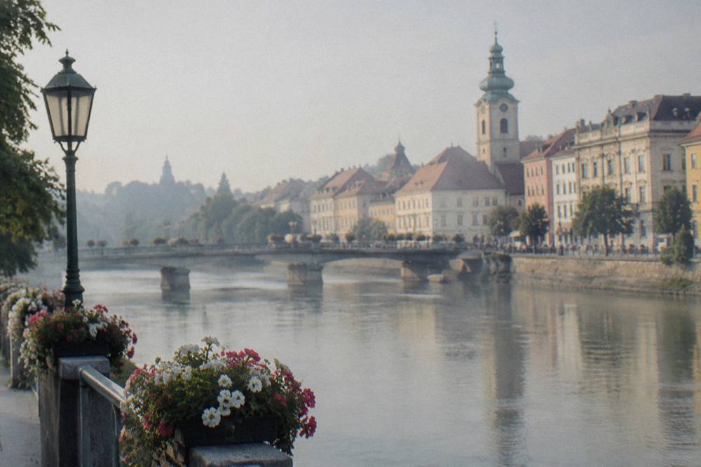 An evening riverbank with lit bridges between two central European cities