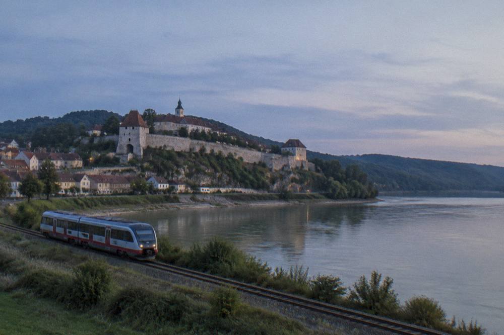 A regional train travelling along a rail line beside the Danube through riverside countryside