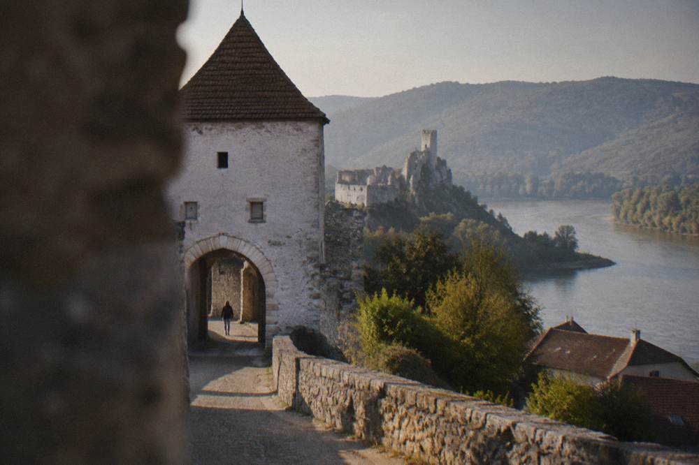 Stone ruins of a castle above a river confluence with forested hills behind