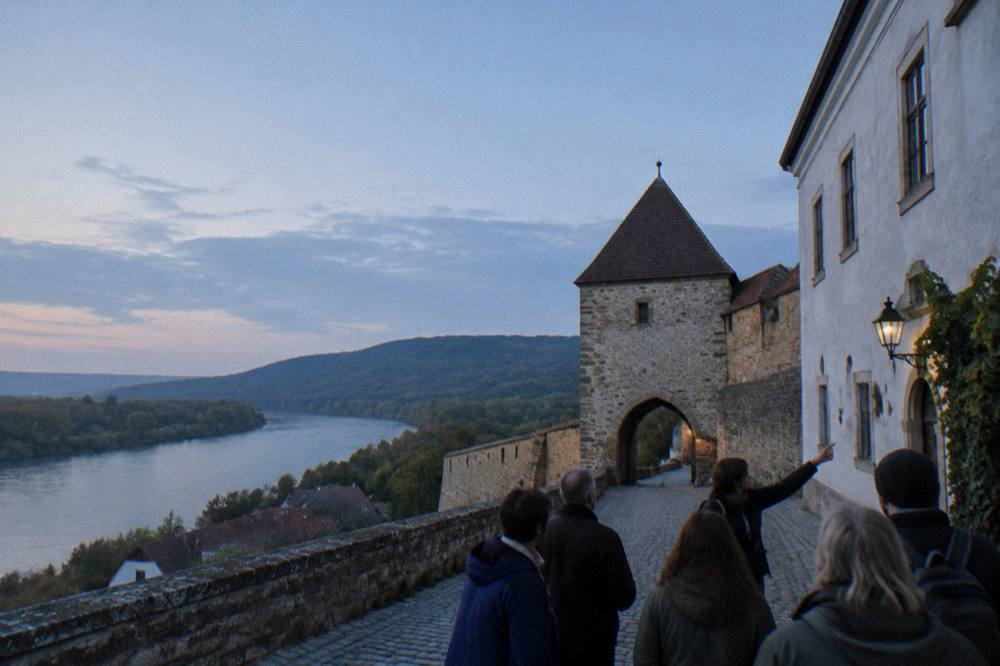 A guided walking group pausing on a cobbled street while a guide points at a building facade