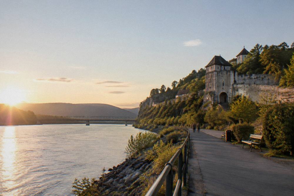 A Danube riverside promenade at golden hour with a bridge in the distance