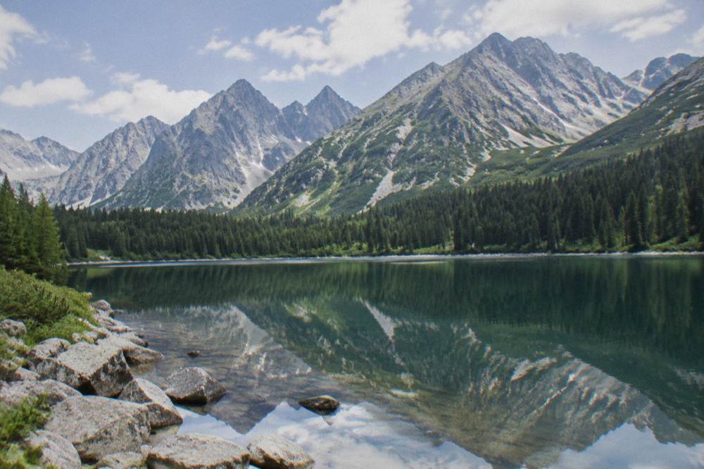 A calm mountain lake reflecting sharp peaks under a partly cloudy sky