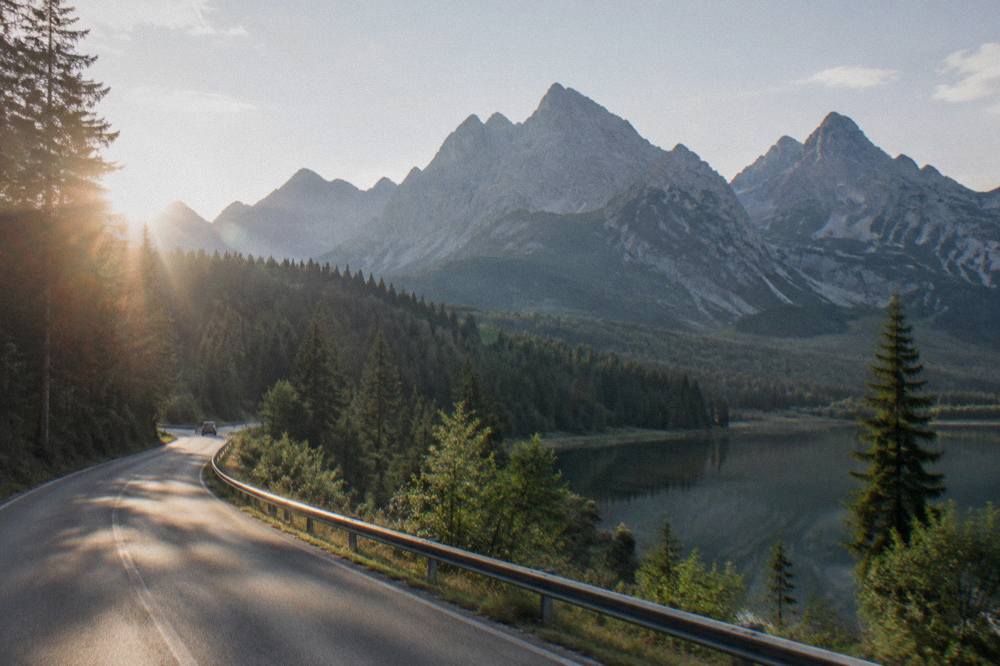 A mountain road winding through forest toward tall rocky peaks