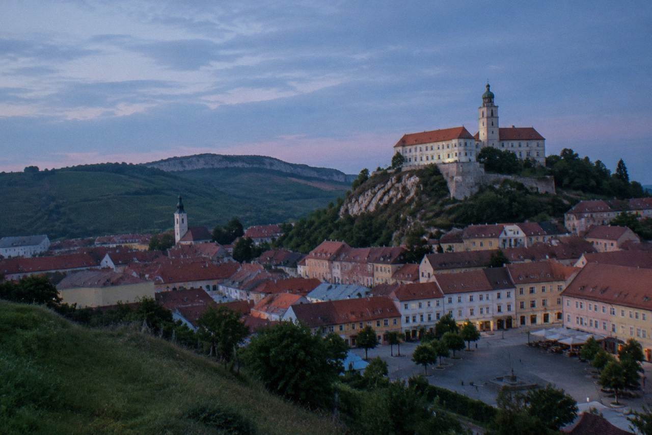A castle on a hill above a small town with red rooftops and a town square below