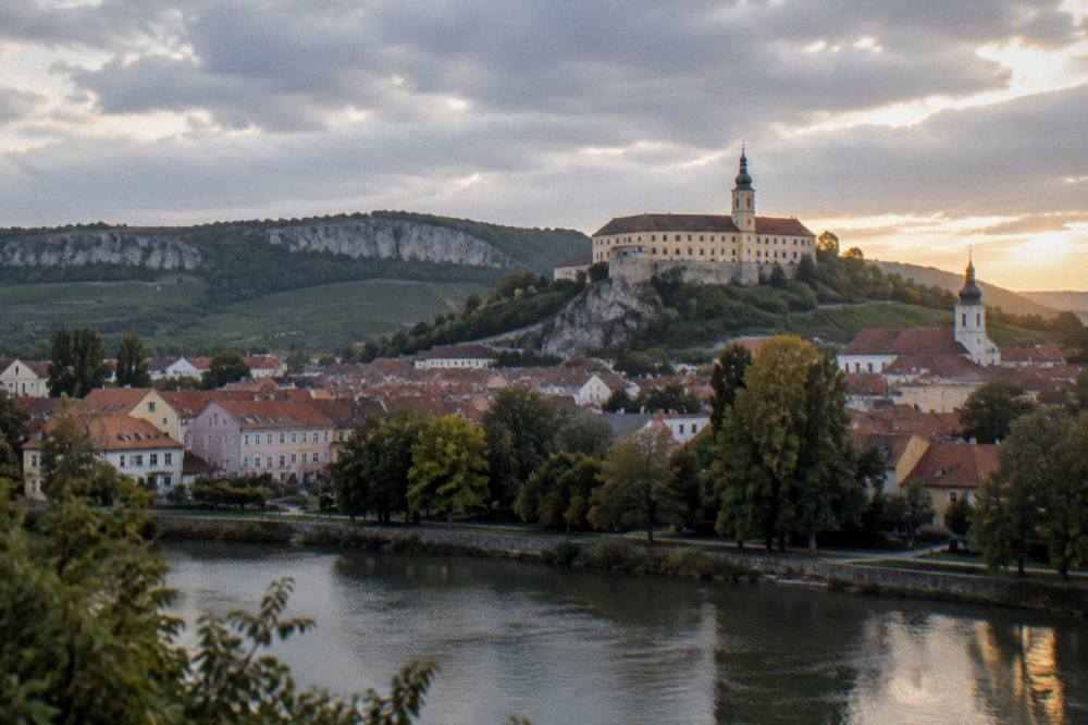 A view over rooftops and a river towards a castle on a hill at dusk