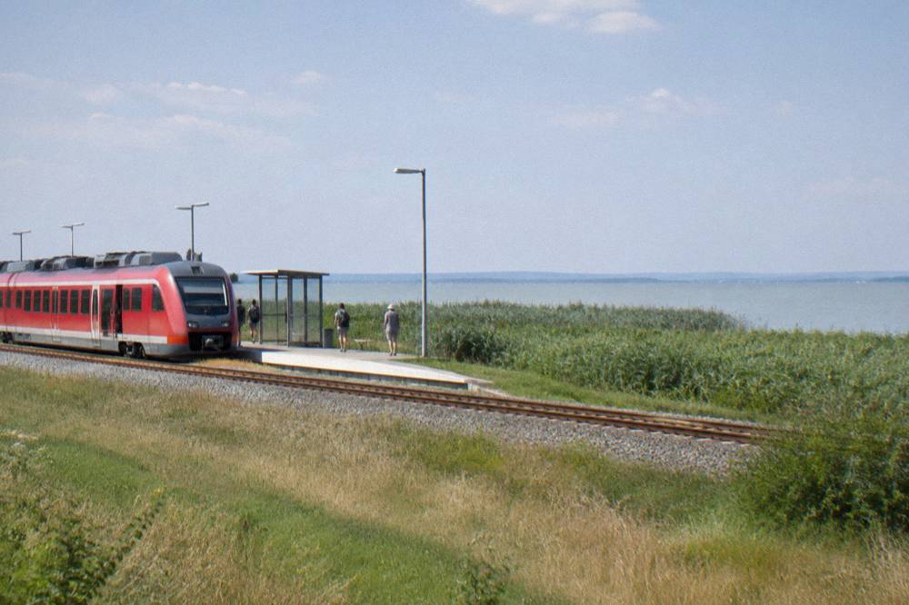 A red regional train stopped at a small station platform beside open countryside