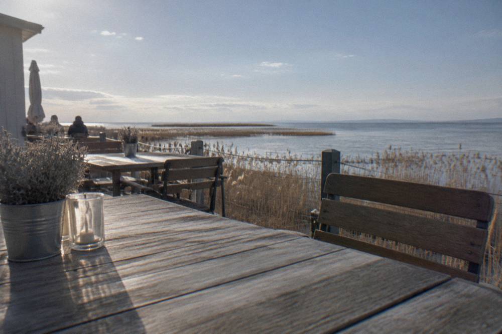 A lakeside terrace with wooden tables and chairs facing the water in bright daylight