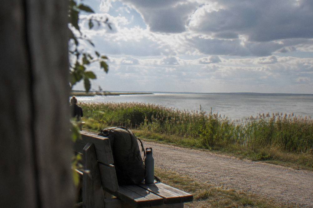 A backpack and water bottle on a wooden bench beside a lakeside path