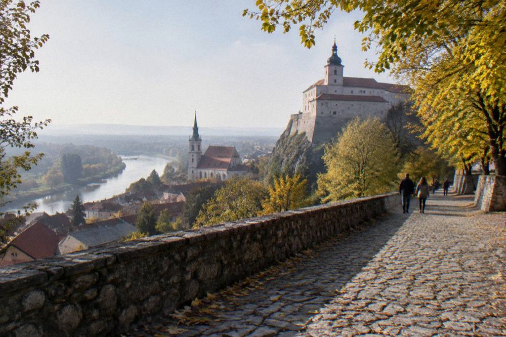 A hilltop castle viewed from a cobbled path lined with trees in autumn colours