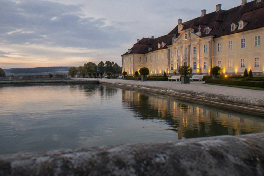 Palace gardens at dusk with the facade lit along a gravel walk