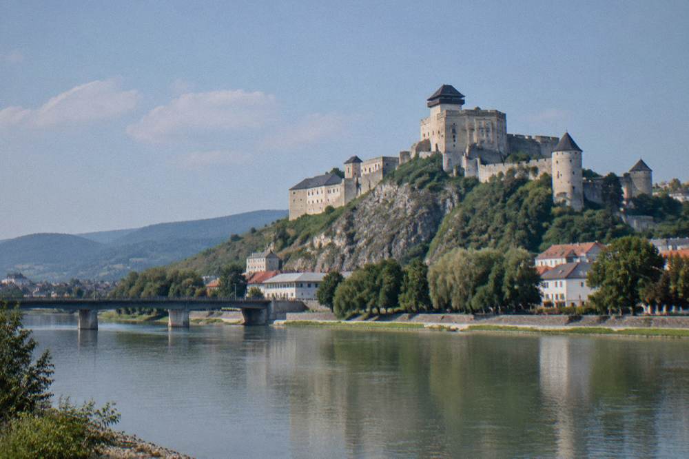 An old stone castle with round towers seen across a river valley