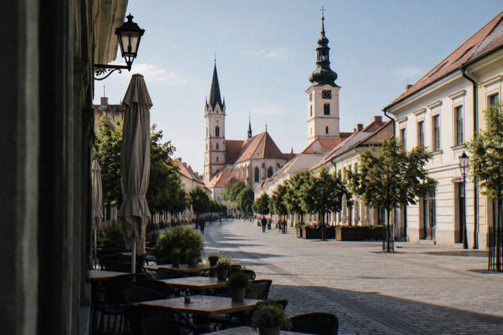 Pedestrian street in a historic Slovak town with outdoor tables and closed facades