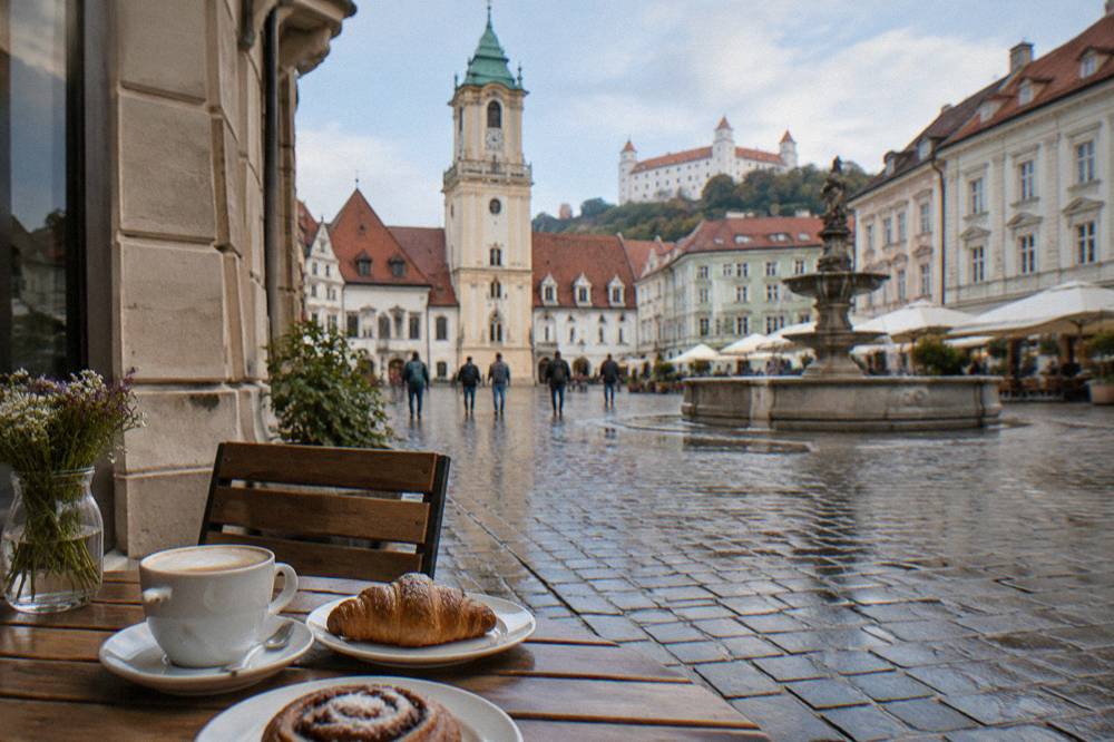 A café table with coffee and pastries beside a historic façade in Bratislava