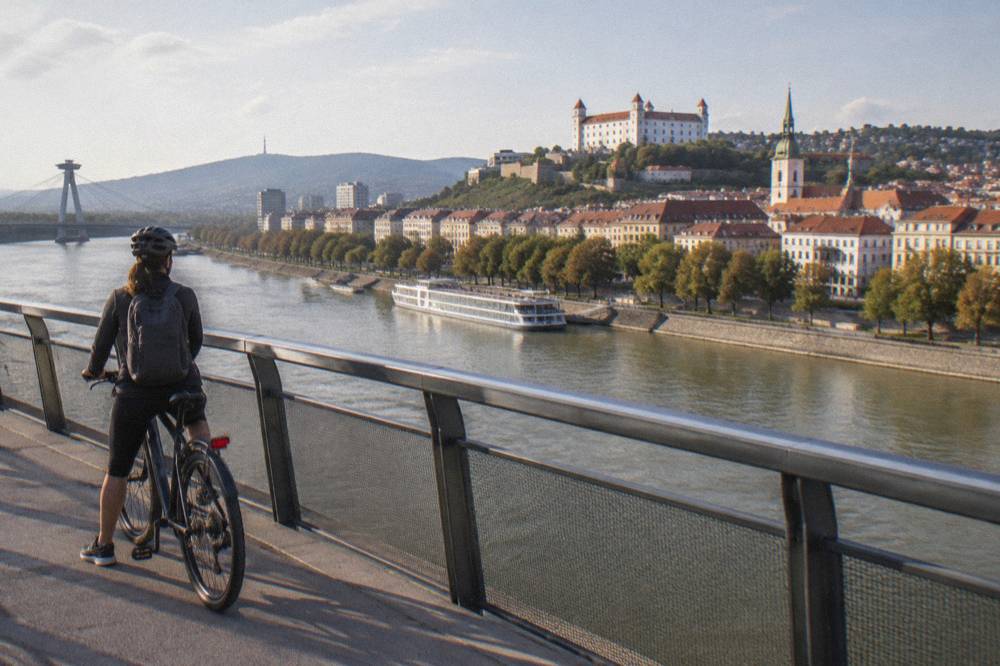 A cyclist pausing on a bridge over the Danube with city rooftops behind