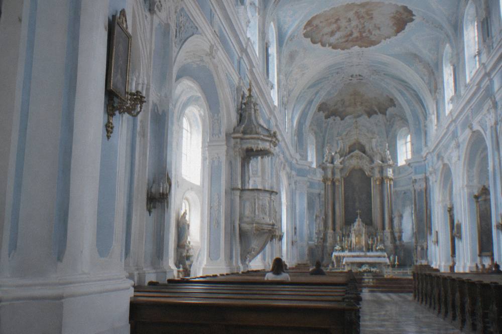 Interior of a blue and white church with a painted ceiling and wooden pews