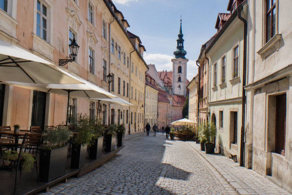 A narrow street in the Bratislava Old Town with pastel facades and a church tower behind
