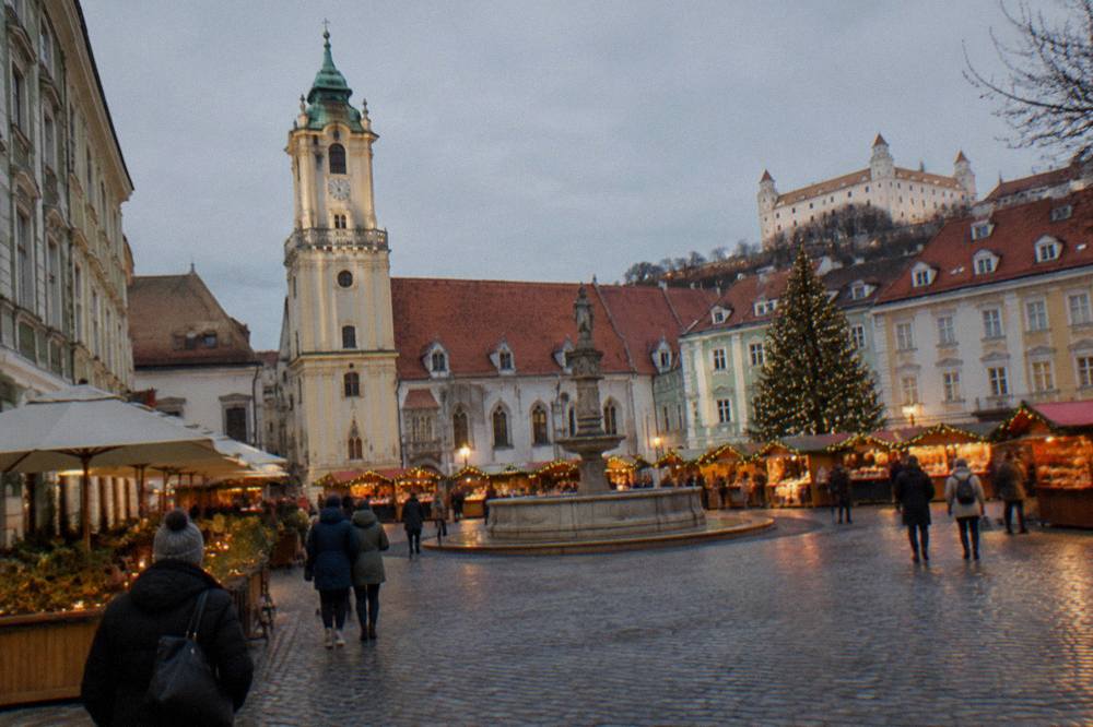 Festive market stalls and lights on a square in Bratislava at dusk