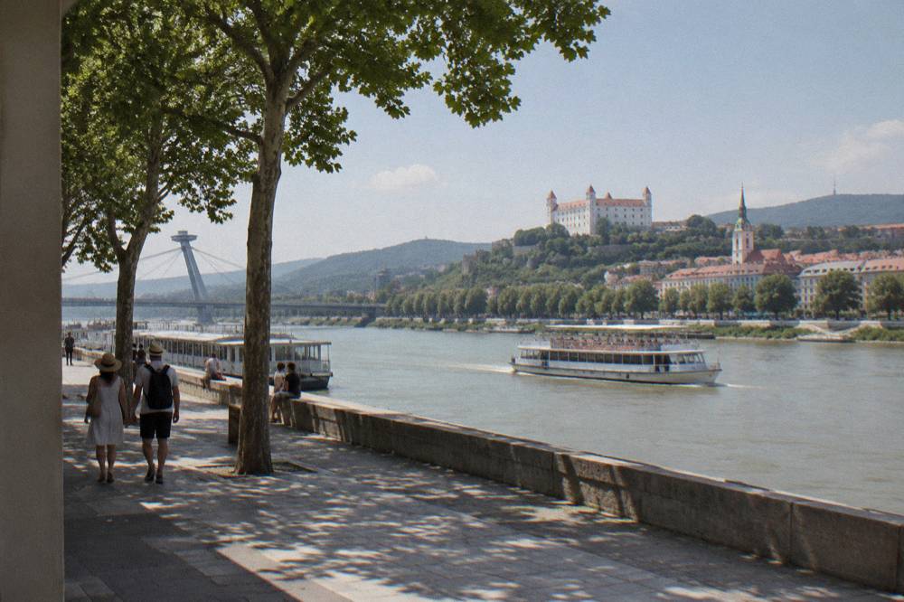 An open-deck river cruise boat on the Danube passing the Bratislava riverfront